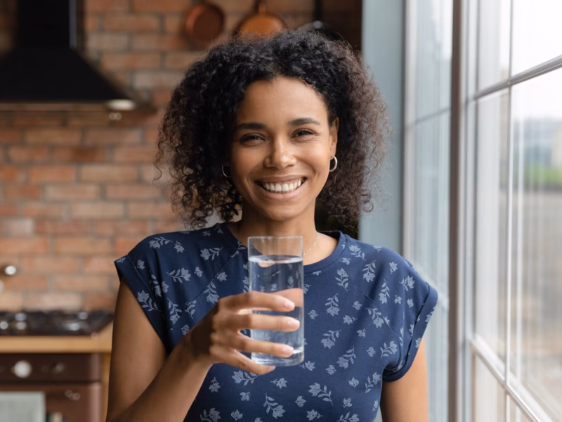 A young multiracial woman in her kitchen drinks pure water produced by her water filtration system