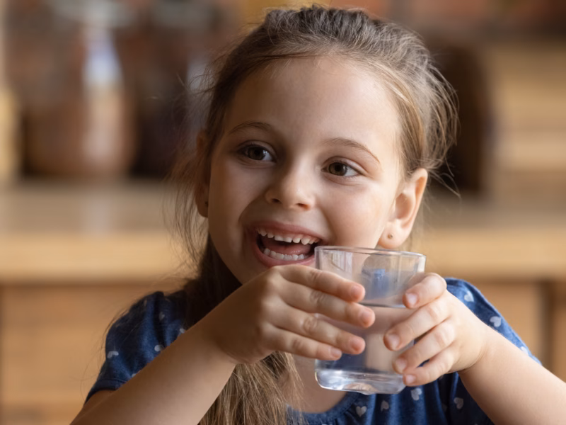A young girl smiles as she drinks water purified to remove PFAS from drinking water