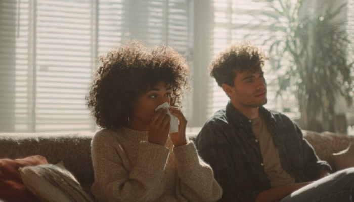 Couple in a Charlottesville, VA home relaxing on a couch during spring, with one person sneezing, suggesting indoor air quality issues from dust and pollen.